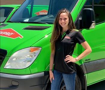 Woman employee standing in front of green truck, long brown hair